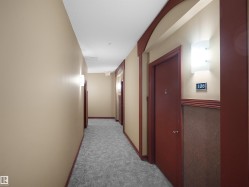 Hallway featuring textured carpeting, beige walls, and dark wood trim - 