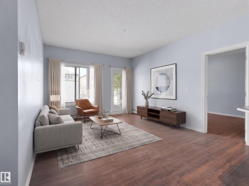 Spacious living area featuring wood-finish flooring, light blue walls, and a large window with a glass paneled door - 106 263 Macewan Road, Edmonton, AB 