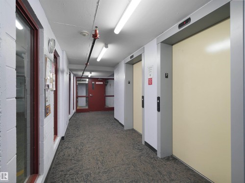 Hallway featuring two elevators with cream-colored doors and grey frames, carpeted flooring, and white painted block walls - 106 263 Macewan Road, Edmonton, AB 