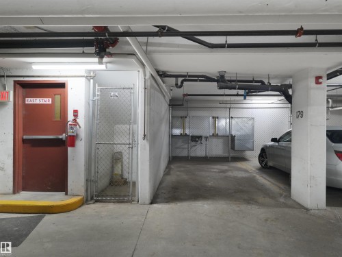 Underground parking area featuring concrete flooring, exposed overhead piping, and fluorescent lighting - 106 263 Macewan Road, Edmonton, AB 