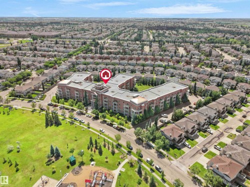 Brick condominium building with multiple balconies, situated alongside a public park featuring a playground and green space - 106 263 Macewan Road, Edmonton, AB 
