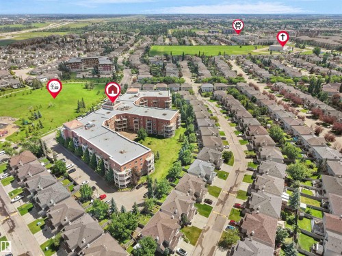 Expansive aerial view showcasing a residential neighborhood with a large condominium building, numerous detached homes, a substantial green space, and visible roadways - 106 263 Macewan Road, Edmonton, AB 