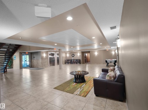 Spacious common area featuring large format tile flooring, recessed lighting, and a prominent open staircase with dark wood treads - 106 263 Macewan Road, Edmonton, AB 