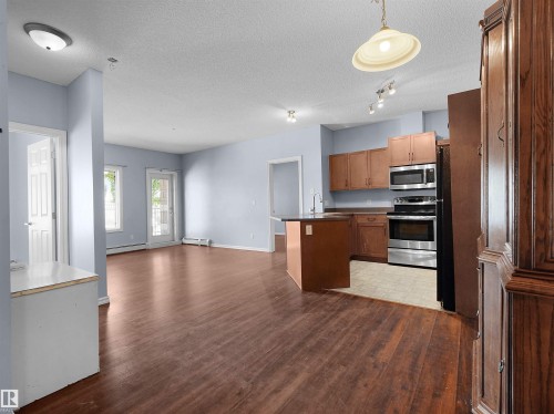 Open-concept main living area featuring dark wood-finish flooring, a kitchen island, stainless steel appliances, and a glass-paneled door - 106 263 Macewan Road, Edmonton, AB 