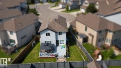 Rear exterior of a two-story residence featuring light gray siding, a brown shingle roof, and a fenced backyard - 