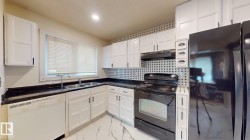Bright kitchen featuring abundant white cabinetry, black appliances, dark countertops, a window over a double-basin sink, and patterned floor tiling - 