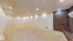 Spacious room with plush carpet flooring, recessed lighting, and a brick accent wall featuring a tiled hearth - 