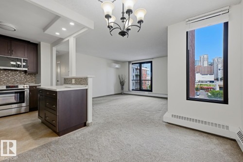 Kitchen and living area featuring dark wood-finish cabinetry, stainless steel appliances, a tiled backsplash, and recessed lighting - 505 10145 109 Street, Edmonton, AB 