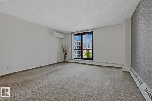 Spacious room featuring textured carpeting and a full-height glass door with a balcony railing - 505 10145 109 Street, Edmonton, AB 