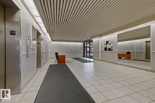 Spacious corridor featuring white tiled flooring, a slatted ceiling, and recessed lighting - 505 10145 109 Street, Edmonton, AB 