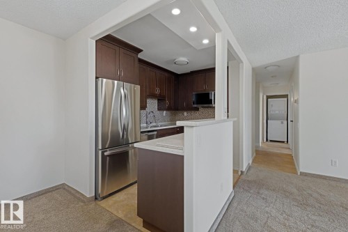 Kitchen featuring dark wood cabinetry, stainless steel appliances, mosaic tile backsplash, and light-toned countertops - 505 10145 109 Street, Edmonton, AB 