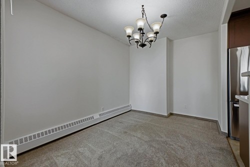 Dining area featuring carpet flooring, a multi-bulb chandelier, and a baseboard heating element - 505 10145 109 Street, Edmonton, AB 