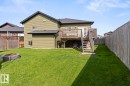 Expansive backyard featuring a manicured lawn, a built-in fire pit, a wooden deck with stairs, a privacy fence, and light green vinyl siding - 35 Falcon Road, Cold Lake, AB 