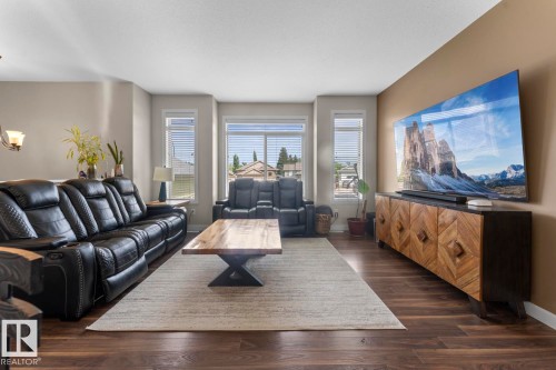 Living area featuring rich wood-finish flooring, light-toned walls, and a large bay window with horizontal blinds - 35 Falcon Road, Cold Lake, AB 