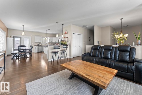 Open-concept living area featuring wood-finish flooring, a kitchen island with seating, pendant lighting, and white cabinetry - 35 Falcon Road, Cold Lake, AB 