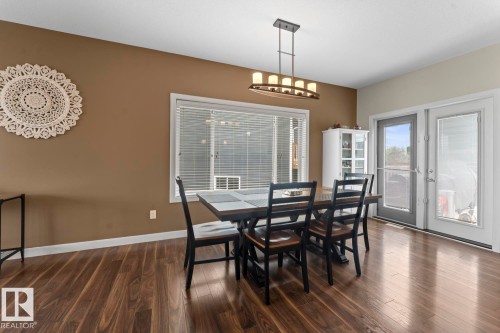 Dining area featuring wood-finish flooring, a contemporary linear chandelier, ample natural light from the large window, and double glass-panel doors - 35 Falcon Road, Cold Lake, AB 