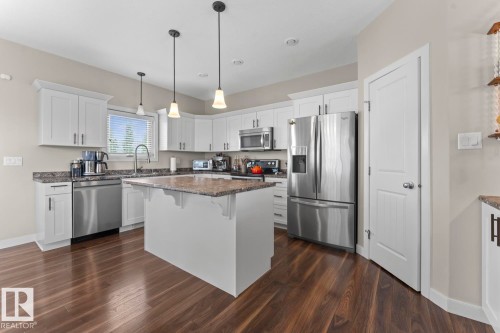 Modern kitchen featuring a central island, white shaker cabinetry, stainless steel appliances, and dark wood-finish flooring - 35 Falcon Road, Cold Lake, AB 