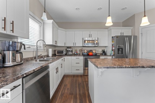 Kitchen featuring white cabinetry, dark wood-finish flooring, a central island with a stone-look countertop, stainless steel appliances, and pendant lighting - 35 Falcon Road, Cold Lake, AB 