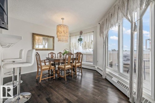 Spacious dining area featuring dark wood-finish flooring, a contemporary chandelier, and large windows with direct outdoor access - 427 15499 Castle Downs Road, Edmonton, AB 