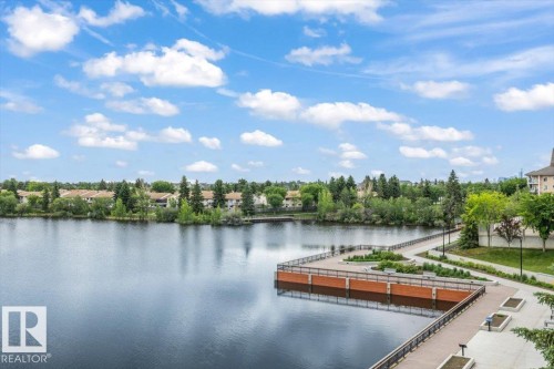 Waterfront promenade featuring a wide paved walkway, metal railings, and integrated planters - 427 15499 Castle Downs Road, Edmonton, AB 