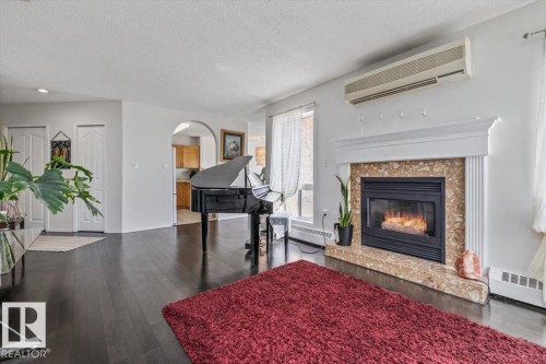 Spacious living area featuring dark wood-finish flooring, a decorative fireplace with a stone surround and white mantel, and an arched doorway leading to a kitchen with wood cabinetry - 427 15499 Castle Downs Road, Edmonton, AB 