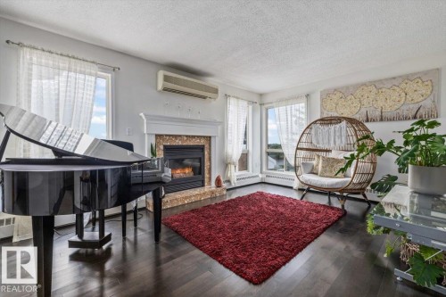Living area with dark wood-finish flooring, a white mantel fireplace with a tiled surround, and multiple windows - 427 15499 Castle Downs Road, Edmonton, AB 