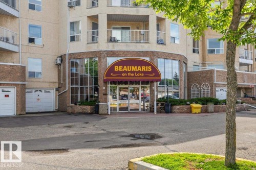 "Beaumaris on the Lake" building entrance featuring a burgundy awning, a curved facade with extensive glazing, and brick accents - 427 15499 Castle Downs Road, Edmonton, AB 