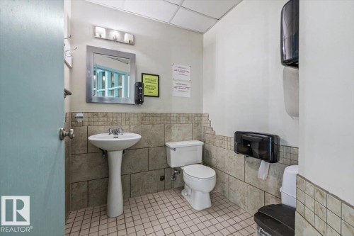 Pedestal sink with chrome fixtures, framed mirror with vanity lighting, tiled walls, and tiled flooring - 427 15499 Castle Downs Road, Edmonton, AB 