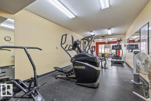 Fitness room featuring a variety of exercise equipment, wall-mounted mirrors, and recessed fluorescent lighting - 427 15499 Castle Downs Road, Edmonton, AB 