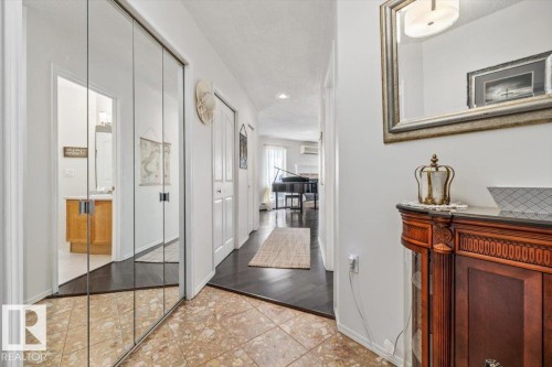 Hallway featuring mirrored closet doors, tile flooring, and wood-finish flooring extending into a bright interior space - 427 15499 Castle Downs Road, Edmonton, AB 