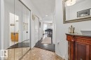 Hallway featuring mirrored closet doors, tile flooring, and wood-finish flooring extending into a bright interior space - 427 15499 Castle Downs Road, Edmonton, AB 