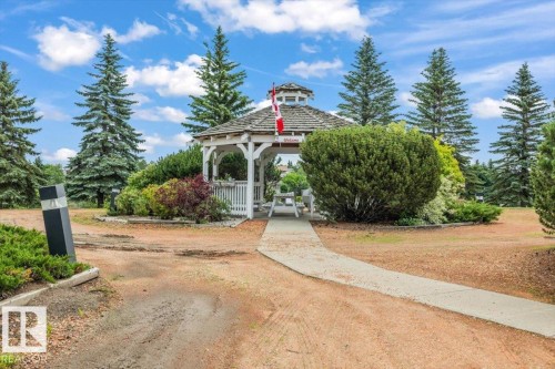White wooden gazebo with a multi-tiered roof, surrounded by mature evergreen trees and varied shrubs - 427 15499 Castle Downs Road, Edmonton, AB 