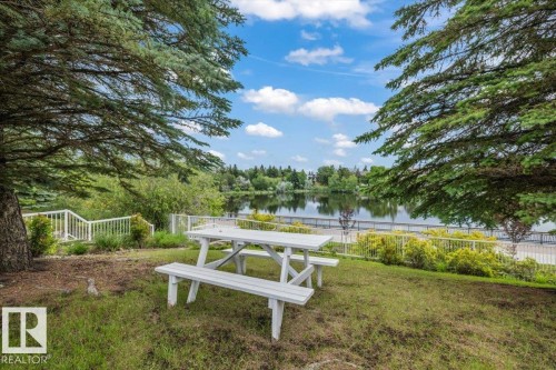 Expansive outdoor area featuring mature evergreen trees, a manicured lawn, and a white wooden picnic table - 427 15499 Castle Downs Road, Edmonton, AB 