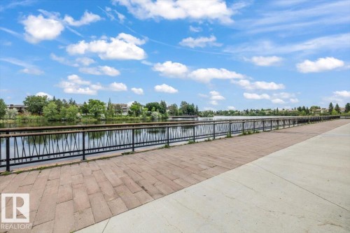 Waterfront pathway featuring a metal railing with wood-finish top, paved with rectangular pavers and concrete - 427 15499 Castle Downs Road, Edmonton, AB 