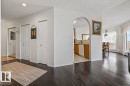 Dark wood-finish flooring extending through the living area, featuring an arched doorway opening to a kitchen with wood cabinetry and a dining area with a large window - 427 15499 Castle Downs Road, Edmonton, AB 