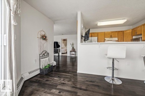 Dark wood-finish flooring throughout, featuring a kitchen peninsula with a breakfast bar, light wood cabinetry, and white walls - 427 15499 Castle Downs Road, Edmonton, AB 