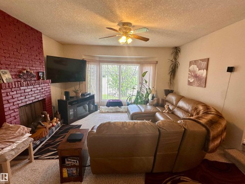 Living area featuring a painted brick fireplace, a ceiling fan with integrated lighting, and a bay window - 10619 108 Avenue, Westlock, AB - Indoor Photo Showing Living Room With Fireplace