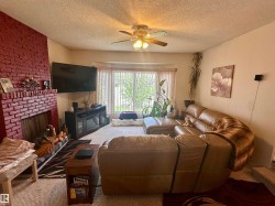 Living area featuring a painted brick fireplace, a ceiling fan with integrated lighting, and a bay window - 