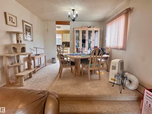 Carpeted dining area featuring a chandelier, a window with vertical blinds, a display cabinet, and a framed wall art piece - 10619 108 Avenue, Westlock, AB - Indoor Photo Showing Dining Room