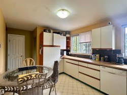 Kitchen featuring an L-shaped counter configuration, white cabinetry with wood-finish accents, and a built-in dishwasher - 