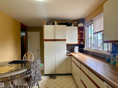 Kitchen area featuring extensive wood-finish countertops, white cabinetry with wood-tone accents, a tiled backsplash, and patterned flooring - 10619 108 Avenue, Westlock, AB - Indoor