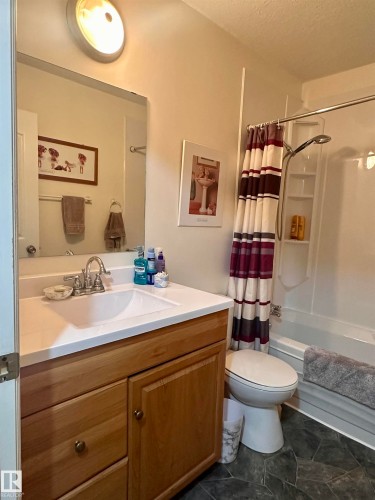 Bathroom featuring a wood-finish vanity with an integrated sink and chrome faucet, a large wall-mounted mirror, and a full shower-tub combination - 10619 108 Avenue, Westlock, AB - Indoor Photo Showing Bathroom