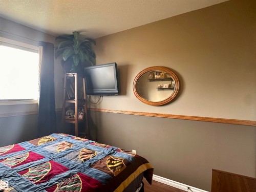 Bedroom featuring a wall-mounted television, wood-finish flooring, and a window with dark drapery - 10619 108 Avenue, Westlock, AB - Indoor Photo Showing Bedroom