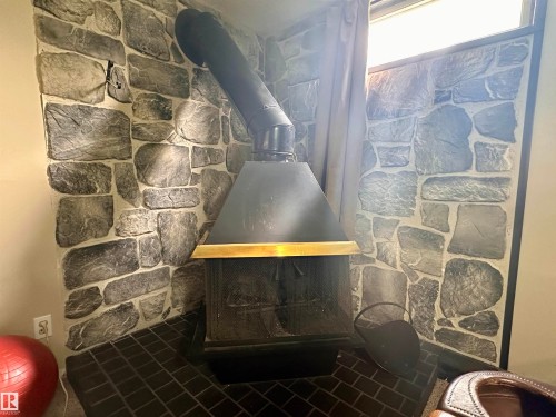 Freestanding fireplace unit with a black metal hood and brass-tone trim - 10619 108 Avenue, Westlock, AB - Indoor