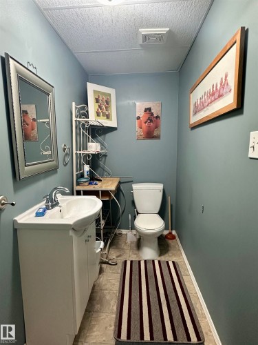 Compact bathroom featuring a white vanity with integrated sink, coordinating toilet, a mirrored medicine cabinet, and light-toned floor tiles - 10619 108 Avenue, Westlock, AB - Indoor Photo Showing Bathroom
