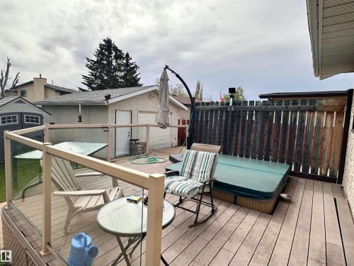 Spacious outdoor deck featuring composite decking, glass panel railing, a built-in hot tub, and a privacy fence - 10619 108 Avenue, Westlock, AB - Outdoor With Deck Patio Veranda With Exterior