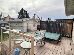 Spacious outdoor deck featuring composite decking, glass panel railing, a built-in hot tub, and a privacy fence - 