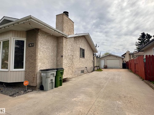 Stucco exterior with brick detailing, featuring a bay window, an attached chimney, and a concrete driveway leading to a detached garage - 10619 108 Avenue, Westlock, AB - Outdoor With Exterior