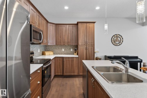 Kitchen with wood-finish cabinetry, stainless steel appliances, and a mosaic tile backsplash - 2007 72 Street, Edmonton, AB - Indoor Photo Showing Kitchen With Double Sink With Upgraded Kitchen