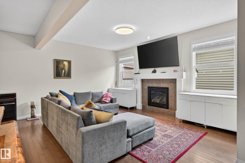 Living area featuring wood-finish flooring, a contemporary fireplace with a tile surround and white mantel, and built-in white cabinetry with countertops flanking the fireplace - 2007 72 Street, Edmonton, AB - Indoor Photo Showing Living Room With Fireplace